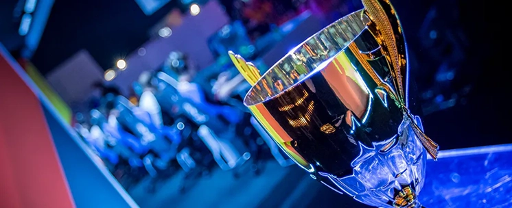 Egy e-sport-bajnokságon egy asztalon álló arany bajnoki trófea, a háttérben elmosódott játékosokkal.